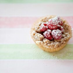Fresh raspberry tart with powdered sugar on pastel striped background.