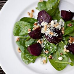 Fresh beet and spinach salad with nuts and crumbled cheese on white plate.