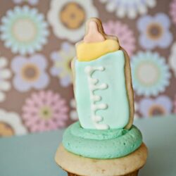 Baby bottle decorated cookie on cupcake with floral background, cute baby shower treat, adorable baby-themed dessert, baby shower cupcake, bakedbree.com.