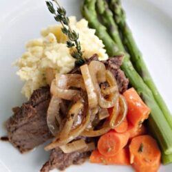 Slow-cooked beef stew with mashed potatoes, carrots, and asparagus on a white plate.