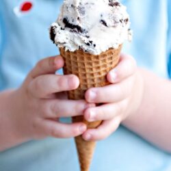 Creamy chocolate chip ice cream in a waffle cone held by a child.
