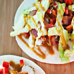 Savory bacon lettuce wrap with vegetables and drizzled sauce on a wooden surface.
