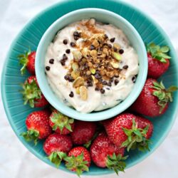 Fresh strawberries with creamy yogurt and crunchy granola topped with chocolate chips and nuts in a turquoise bowl.