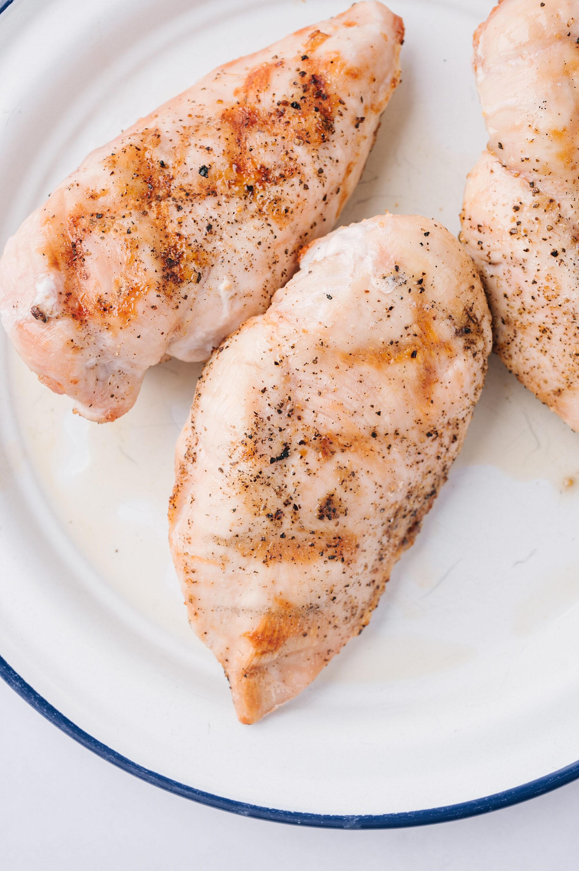 Juicy baked chicken breasts seasoned with herbs and spices on a white plate.