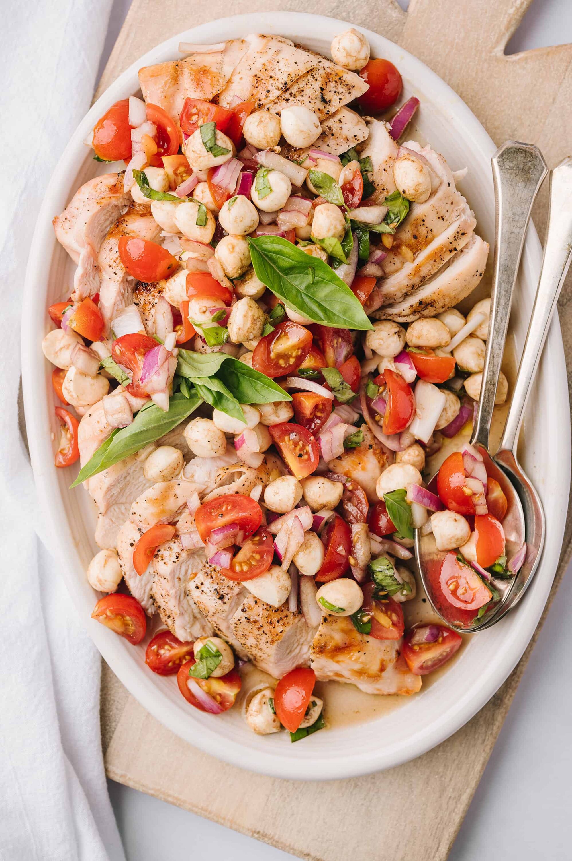 Boneless chicken breast with cherry tomato, basil, and chickpea salad on white oval platter.