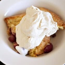 Creamy peach cobbler with whipped cream dessert on white plate.