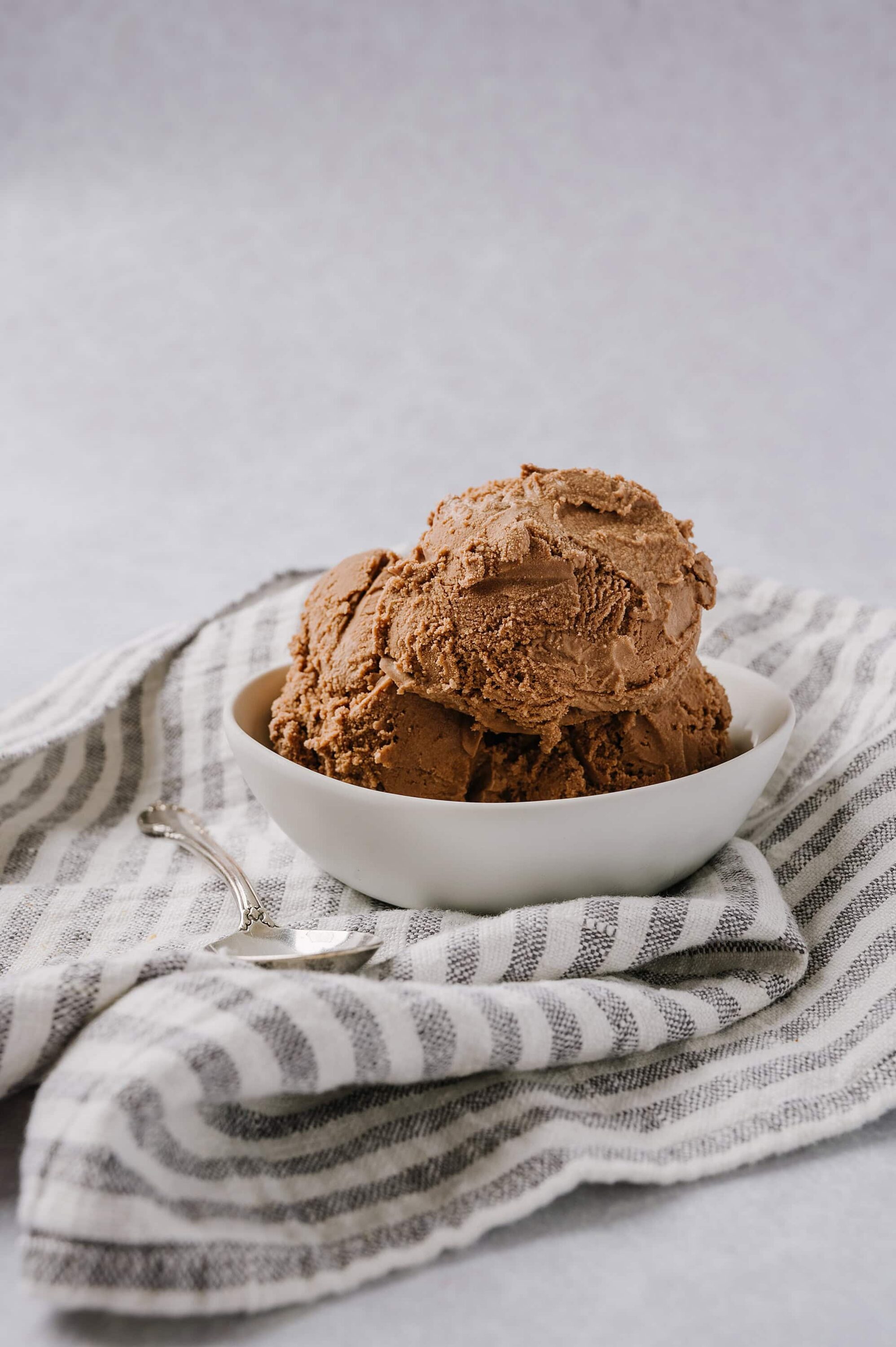 Creamy chocolate ice cream scoops in a white bowl on striped cloth, ideal for dessert recipes.