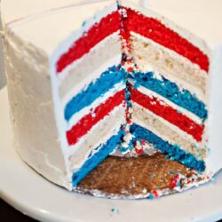 Vibrant red, white, and blue layered patriotic cake with colorful stripes and creamy frosting.