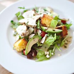 Fresh Caesar salad with grilled chicken, croutons, lettuce, avocado, and Parmesan cheese on white plate.