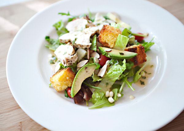 Fresh Caesar salad with grilled chicken, croutons, lettuce, avocado, and Parmesan cheese on white plate.