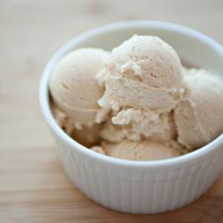 Creamy vanilla ice cream scoops in a white ramekin on a wooden surface.