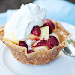 Fresh fruit tart with raspberries, pineapple, and whipped cream on a white plate.