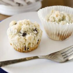 Fresh blueberry muffin with crumbly topping on a white plate, bakery-style baked good.