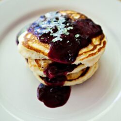 Fluffy pancakes topped with blueberry syrup on a white plate.