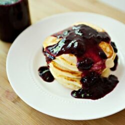 Fluffy pancakes topped with mixed berry sauce on a white plate.