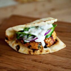 Crispy chicken shawarma pita with fresh vegetables and creamy tahini sauce on a wooden cutting board.