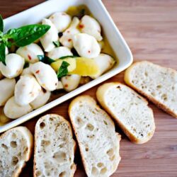Creamy mozzarella and basil salad with olive oil served with rustic baguette slices on a wooden table, perfect for appetizers.