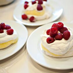 Fresh raspberry-topped pavlova dessert on white plates.