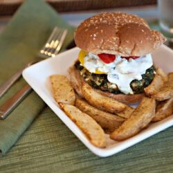 Crispy vegetarian burger with potato wedges on white plate in cozy dining setting.