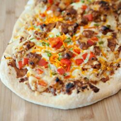 Fresh homemade taco pizza topped with seasoned beef, cheese, and vegetables on a wooden board.