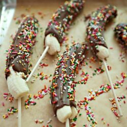 Banana pops dipped in chocolate with colorful sprinkles, served as fun and delicious treats.