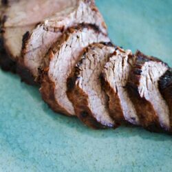 Juicy sliced roasted pork tenderloin on a teal plate.