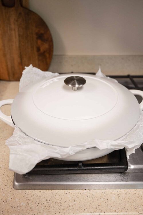 Steaming a white ceramic Dutch oven with parchment paper on stovetop, ready for baking.