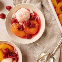 Fresh peach and raspberry dessert with a scoop of vanilla ice cream in a white bowl.