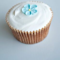 Delicious vanilla cupcake with white frosting and blue flower decoration.