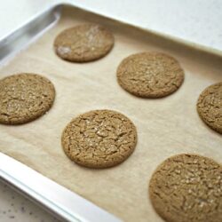 Golden brown ginger cookies baking on a parchment-lined tray. Perfect for holiday treats and homemade cookies.