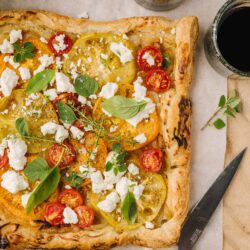 Fresh homemade tomato and basil tart with feta cheese, served with glasses of red wine.