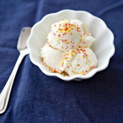 Creamy vanilla ice cream with colorful sprinkles in a white bowl on dark blue background, perfect for homemade ice cream recipes.