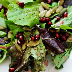 Fresh mixed green salad with pomegranate seeds and pumpkin seeds, healthy vegan side dish.