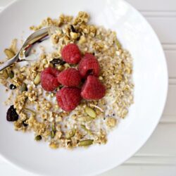 Fresh raspberry granola bowl with yogurt and mixed nuts on a white plate.