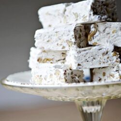 Creamy white chocolate almond bark stacked on a glass cake stand, perfect for homemade candy treats.