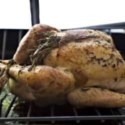 Roasted whole chicken with herbs on a baking rack.