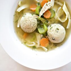 Creamy vegetable and meatball soup with carrots, celery, and pasta in a white bowl.