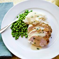 Juicy stuffed chicken breast with creamy gravy and green peas on white plate.