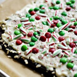 Festive holiday bark with peppermint candies, red and green M&Ms, and white chocolate drizzle on a baking sheet.