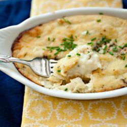 Creamy homemade mashed potatoes with melted cheese and chives, served in a white casserole dish.