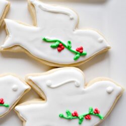 Decorated holiday dove cookies with white icing and red and green holly accents.