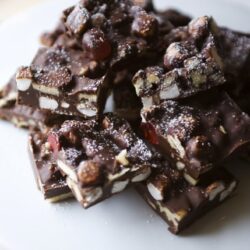 Chunky homemade chocolate bark with nuts and dried fruits on a white plate.
