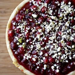 Fresh cherry and white chocolate dessert pizza on wooden surface, baked Bree style.