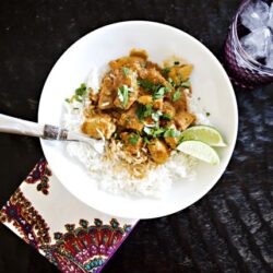 Rich beef curry served over fluffy white rice with lime wedges and fresh herbs on a dark wooden table.