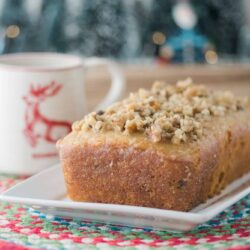 Homemade carrot cake slice with chopped nuts on top, served on a white plate with a festive tablecloth.
