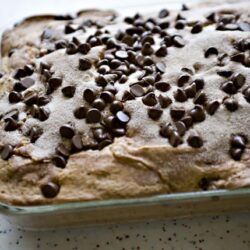 Chocolate chip cookie sheet dessert in glass baking dish, freshly baked and topped with chocolate chips.