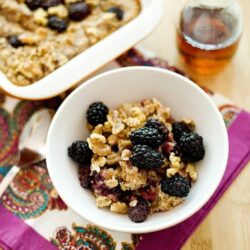 Fresh blackberry crumble baked oatmeal in a white bowl on colorful cloth.