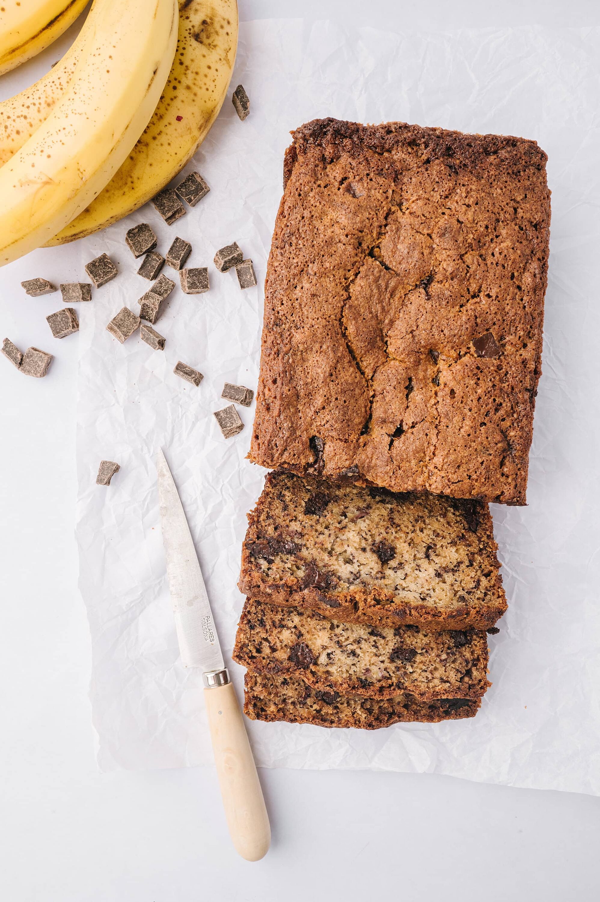 Banana bread with chocolate chips on white parchment paper, sliced for serving.