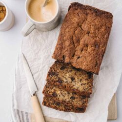 Moist chocolate chip banana bread with a crispy crust, served on parchment paper with coffee and sugar in the background.