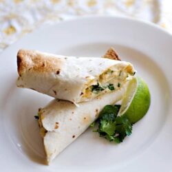 Cream cheese and herb chicken burrito on white plate with lime and cilantro.